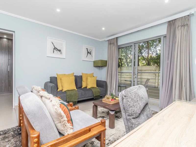 A bright and well-maintained living room featuring tiled floors, recessed lighting, and direct access to a private balcony through sliding glass doors.