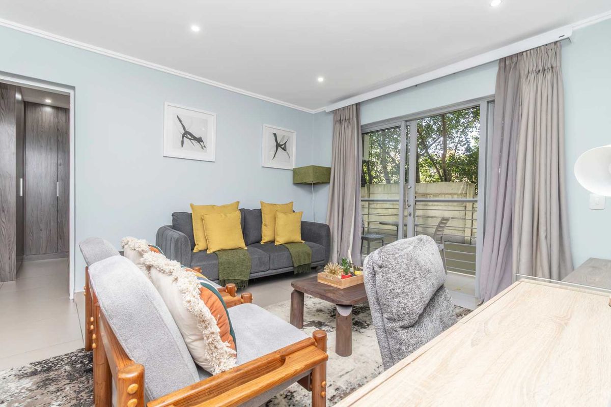 A bright and well-maintained living room featuring tiled floors, recessed lighting, and direct access to a private balcony through sliding glass doors.
