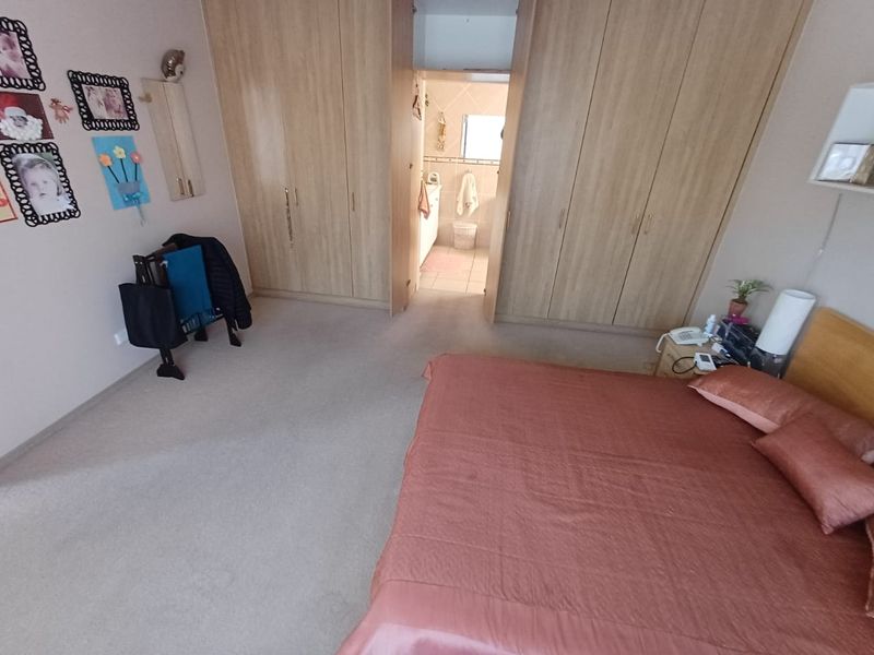 Spacious bedroom featuring extensive built-in wooden cupboards and direct access to an en-suite bathroom.