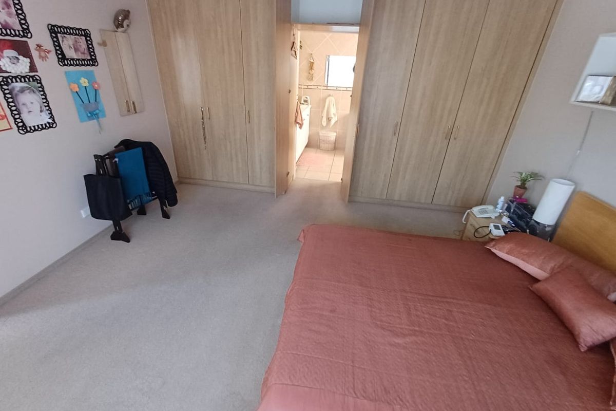 Spacious bedroom featuring extensive built-in wooden cupboards and direct access to an en-suite bathroom.
