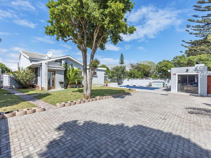 Spacious rear exterior featuring a paved driveway, landscaped garden, swimming pool, and a detached garage structure.