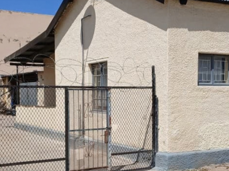 Exterior view of the property featuring a corrugated metal roof, secure chain link fencing with razor wire, and a concrete driveway.