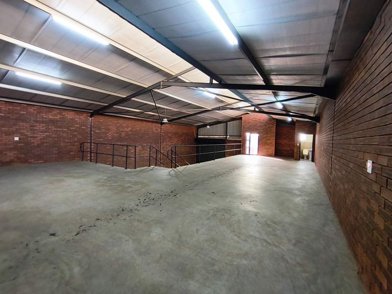 Spacious industrial mezzanine area featuring exposed brick walls, concrete flooring, and high-clearance steel roof trusses with integrated lighting.