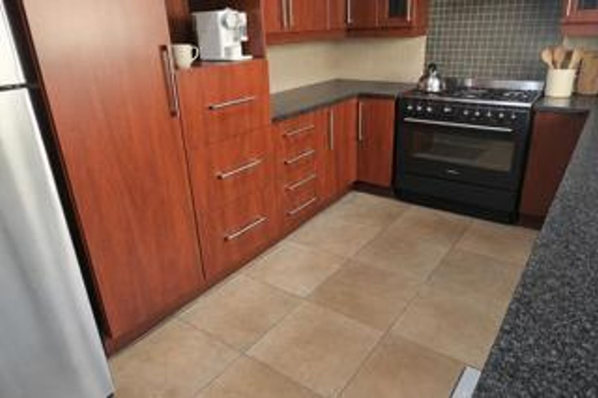 A functional kitchen featuring warm-toned wooden cabinetry, dark granite countertops, a gas stove with oven, and neutral tiled flooring.