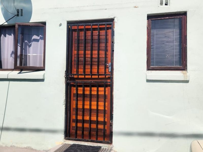 Front elevation of a residential property featuring a timber entrance door with a security gate and aluminium window frames.