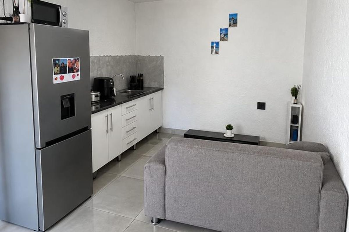 Compact open-plan living area featuring a modern kitchenette with white cabinetry, tiled flooring, and a functional layout suitable for efficient living.
