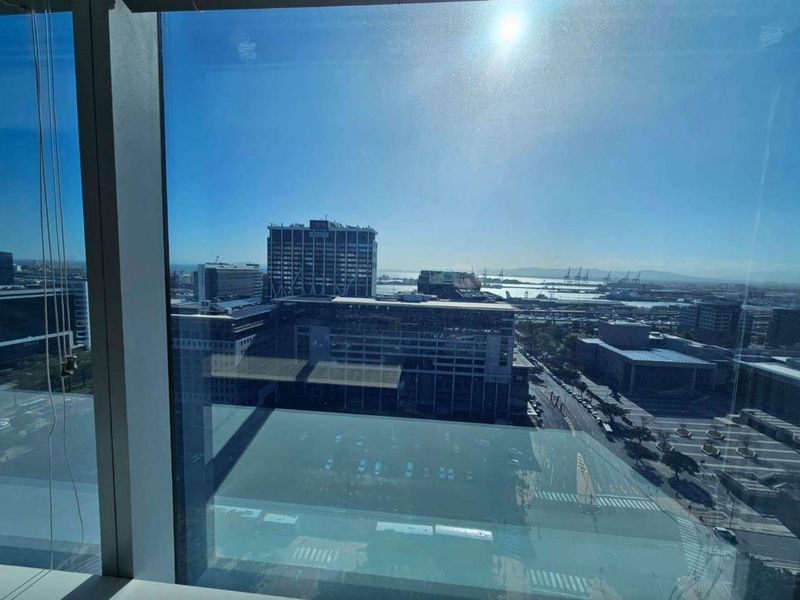 A high-rise office view overlooking the city skyline and harbor through large floor-to-ceiling windows.
