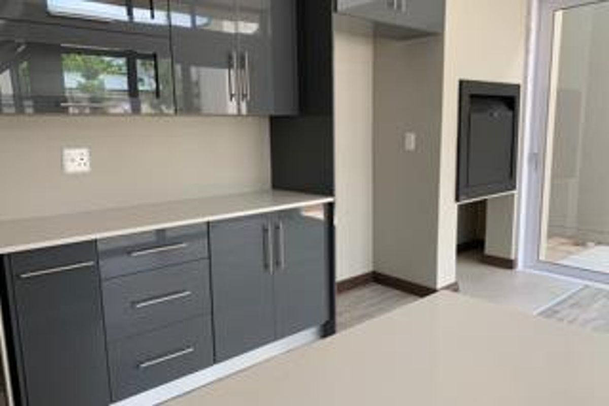 Modern kitchen featuring sleek grey cabinetry, stone countertops, and a built-in braai, with direct access to an outdoor area through a glass door.