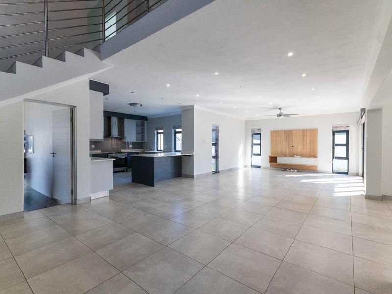Spacious open-plan living and kitchen area featuring large format floor tiles, modern cabinetry, a central island, and a feature staircase with metal railings.