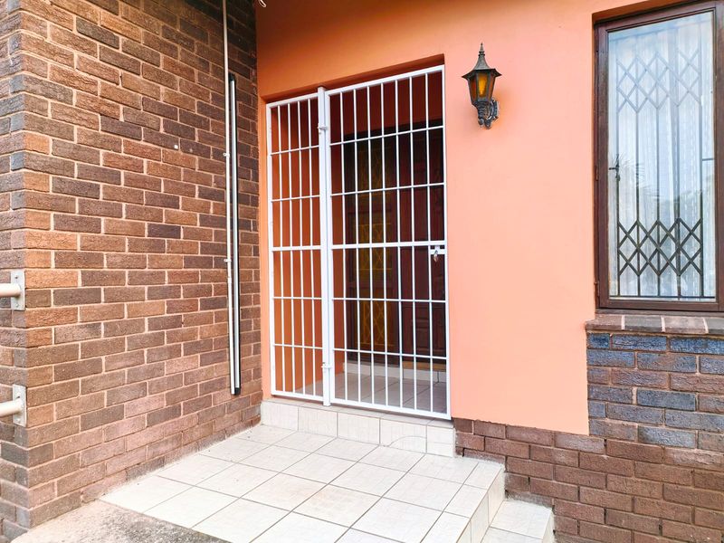 Front entrance area featuring a tiled porch, brick exterior walls, and a white security gate protecting the main door.