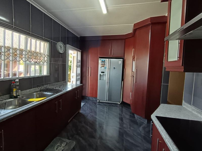 A functional kitchen featuring dark wood cabinetry, tiled walls, and flooring, equipped with a double sink and integrated extractor fan.