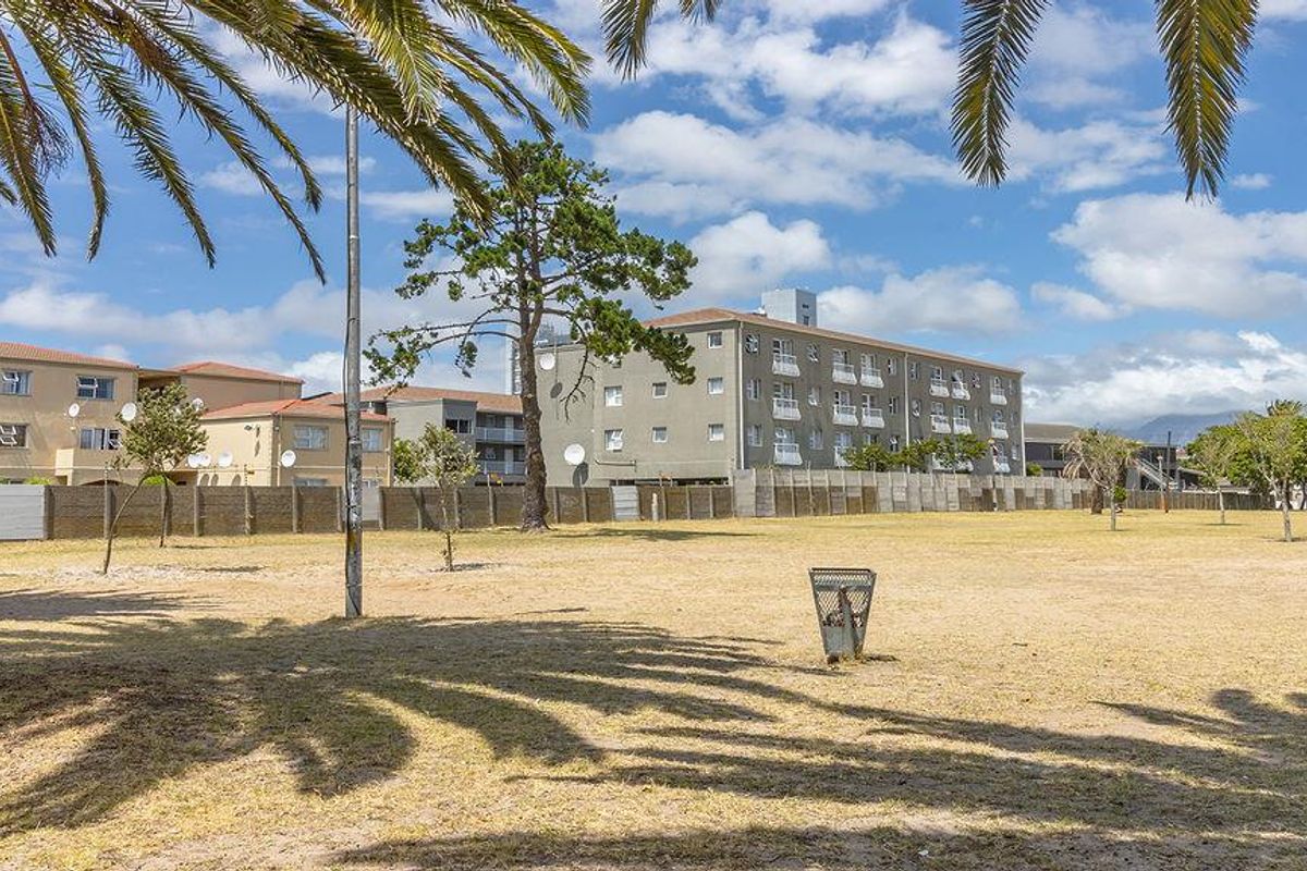 A view of the apartment complex exterior from the adjacent open grass area, featuring multi-story residential buildings with balconies.