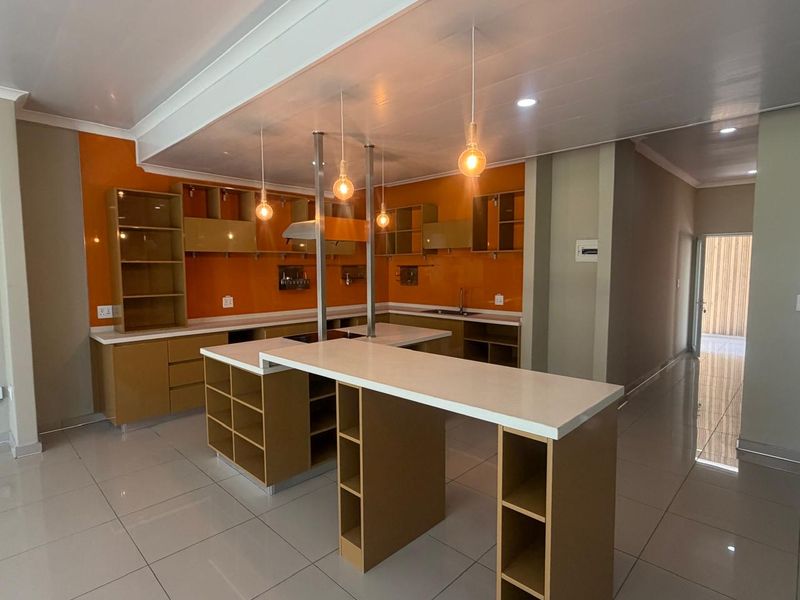 Modern kitchen featuring vibrant orange splashbacks, extensive built-in cabinetry, a central island with breakfast bar seating, and sleek tiled flooring.