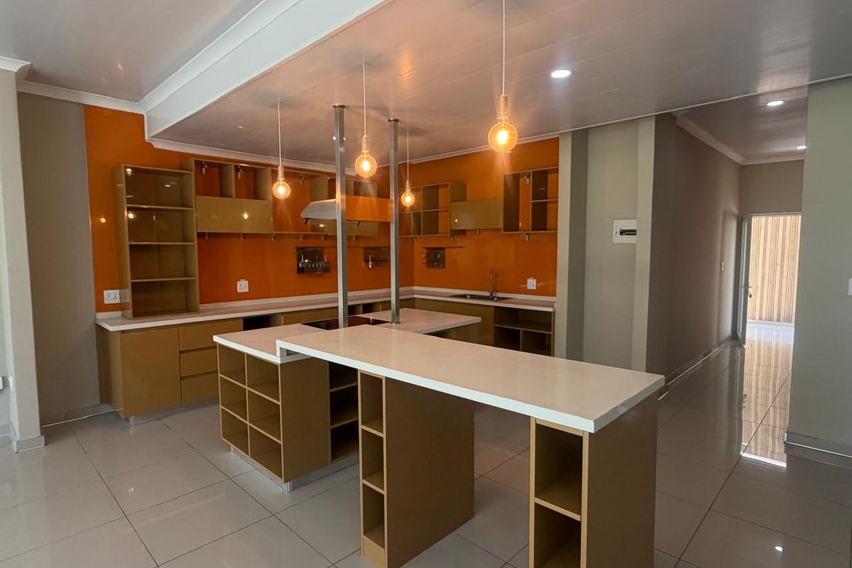 Modern kitchen featuring vibrant orange splashbacks, extensive built-in cabinetry, a central island with breakfast bar seating, and sleek tiled flooring.