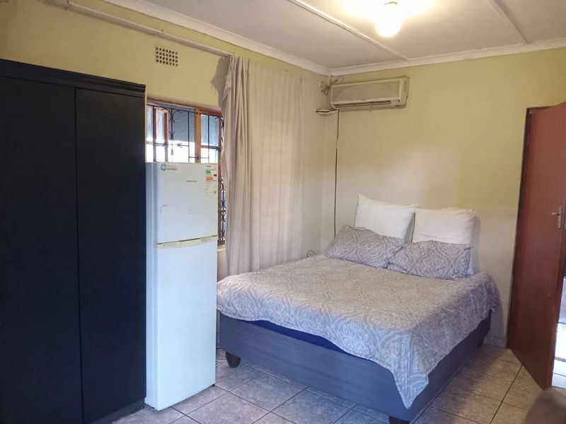 A functional bedroom featuring tiled flooring, an installed air conditioning unit, and security bars on the window.