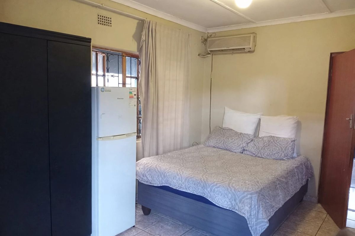 A functional bedroom featuring tiled flooring, an installed air conditioning unit, and security bars on the window.