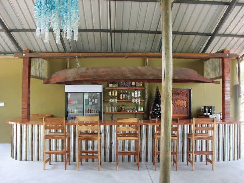 An outdoor bar area featuring a rustic corrugated metal counter, wooden structural supports, and open-air roof design, ideal for guest house entertainment.