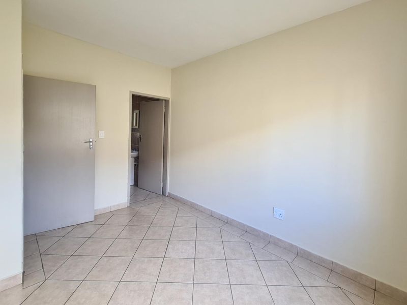 A clean, empty bedroom featuring neutral wall paint, tiled flooring, and direct access to an adjoining bathroom.