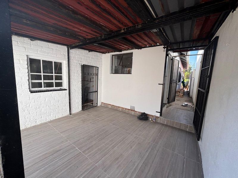 A covered outdoor patio area featuring tiled flooring, security gates, and painted brick walls, providing a functional transition space to the rear of the property.