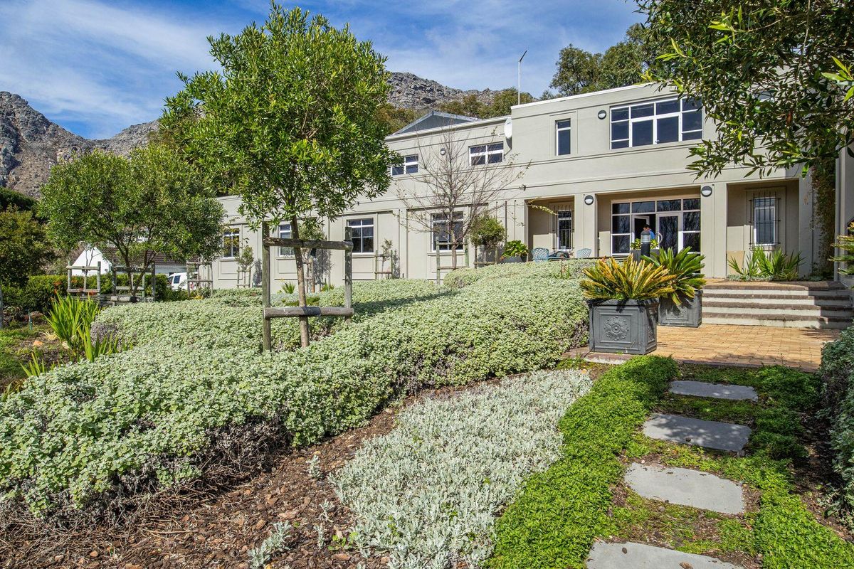 A well-maintained office building exterior featuring a landscaped garden, stone pathway, and paved entrance area set against a mountain backdrop.