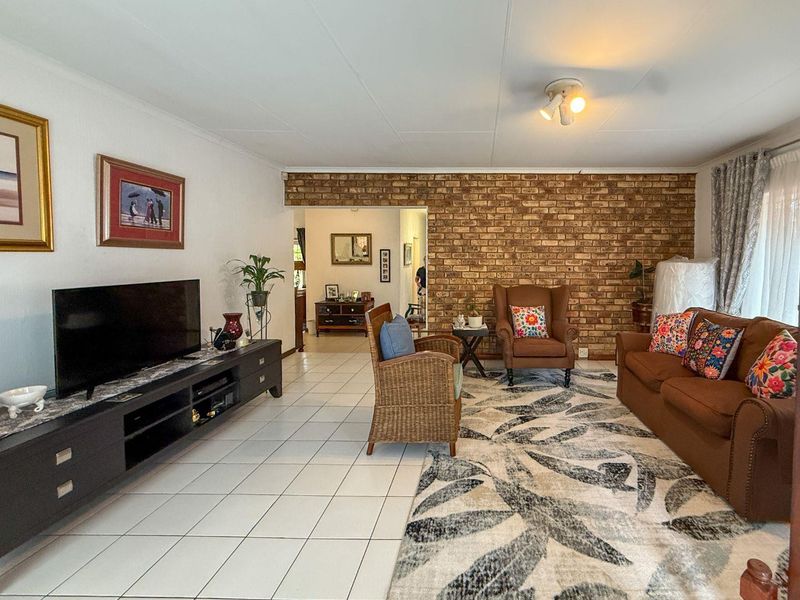 Spacious living room featuring a prominent exposed brick feature wall and neutral ceramic floor tiles, offering a comfortable and functional living space.