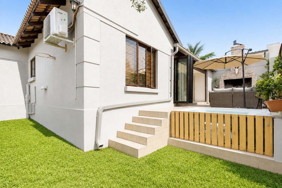 Rear exterior view featuring a small plunge pool with timber decking, tiled steps, and a built-in outdoor fireplace on the patio.