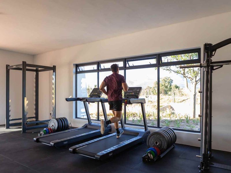 A modern, well-lit home gym featuring large windows with views, tiled flooring, and ample space for fitness equipment.