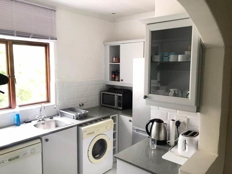 Compact kitchen featuring white cabinetry, subway tile backsplash, stone countertops, and integrated laundry facilities, offering a functional and efficient workspace.