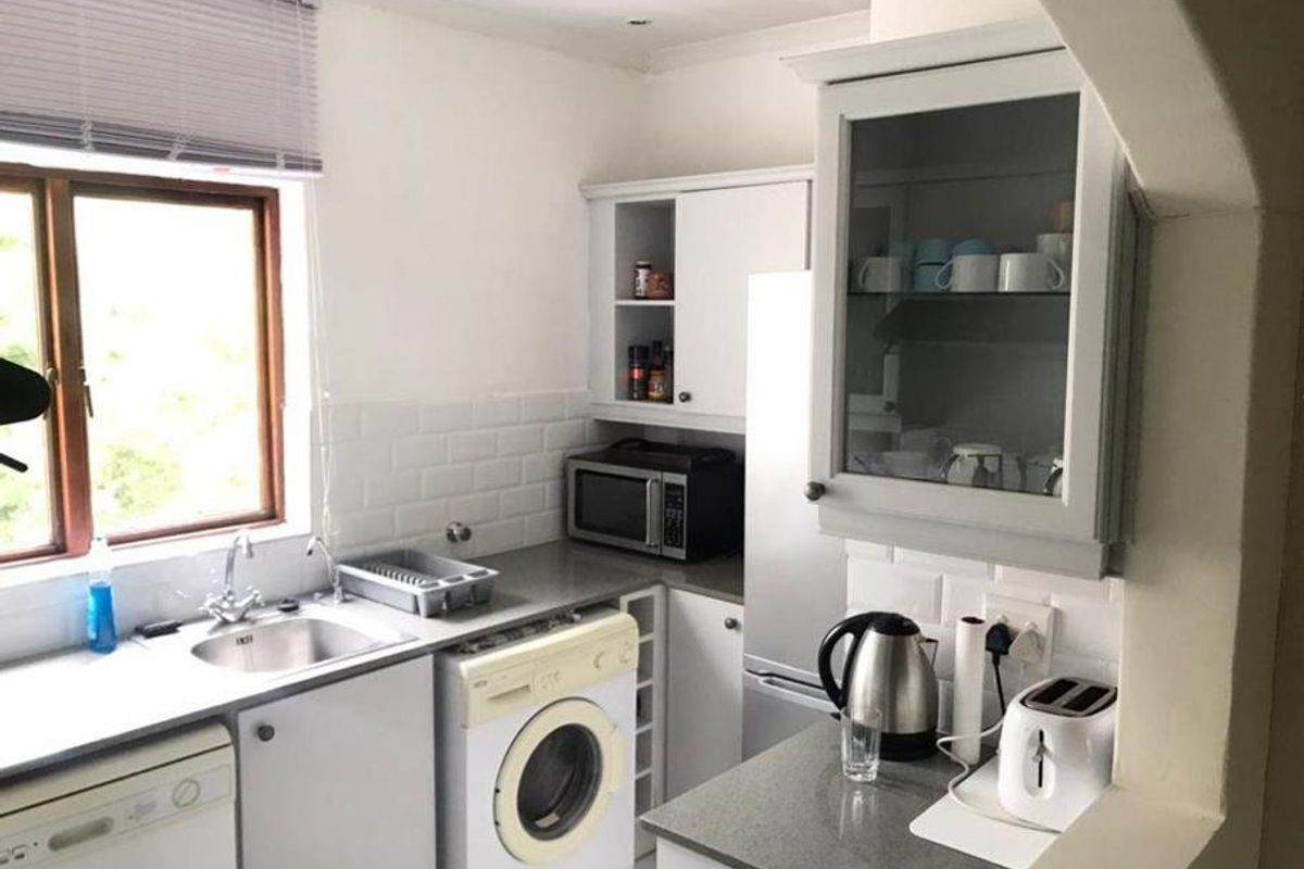 Compact kitchen featuring white cabinetry, subway tile backsplash, stone countertops, and integrated laundry facilities, offering a functional and efficient workspace.