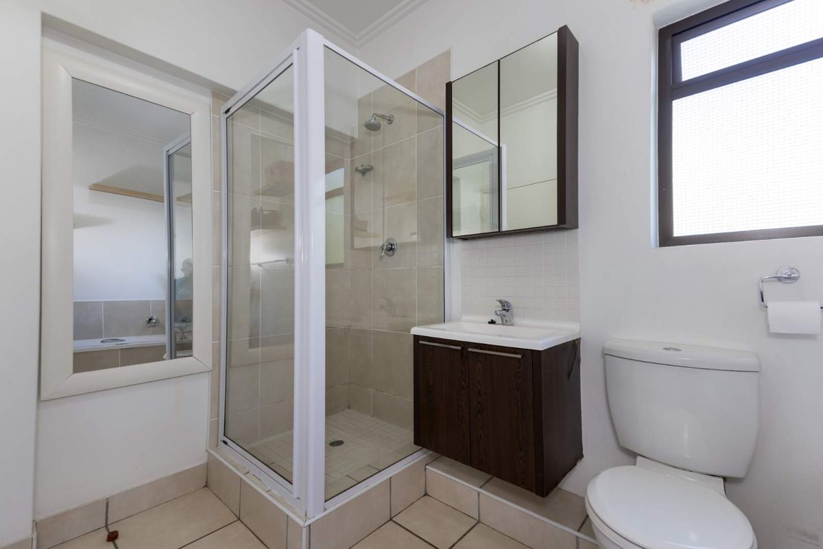 A functional bathroom featuring a glass shower enclosure, wall-mounted vanity with basin, mirrored cabinet, and a standard toilet with tiled finishes.