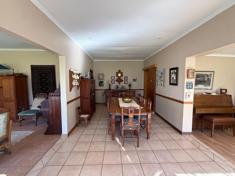 Spacious dining room featuring ceramic floor tiles, a wooden dado rail, and recessed lighting, connecting to adjacent living areas in an open-plan layout.