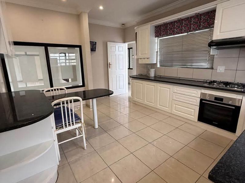 A well-maintained kitchen featuring granite countertops, built-in cabinetry, a gas hob, and an integrated oven with tiled flooring throughout.