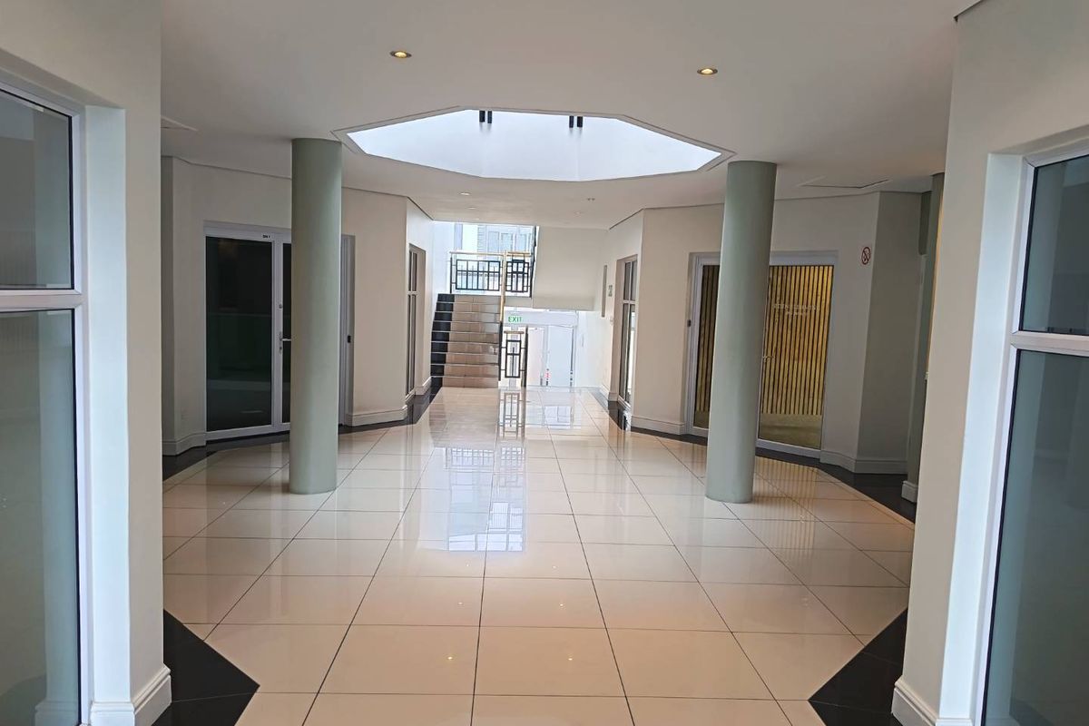 Spacious commercial lobby or hallway featuring polished tile flooring, structural support columns, a central skylight, and a staircase leading to an upper level.