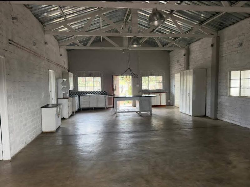 Spacious open-plan area featuring industrial-style exposed steel roof trusses, polished concrete floors, and a functional kitchen layout with a central island.