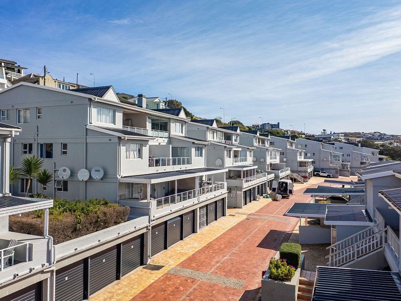 An elevated view of a modern apartment complex featuring multiple levels, private balconies, and a paved driveway with integrated garage access.
