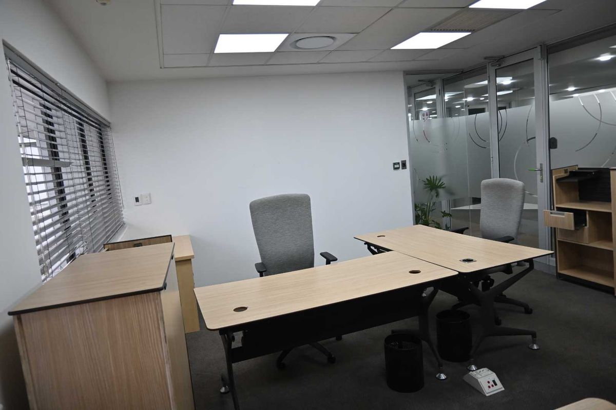 A professional office space featuring a suspended ceiling with recessed lighting, carpeted flooring, and a glass partition wall with privacy frosting.