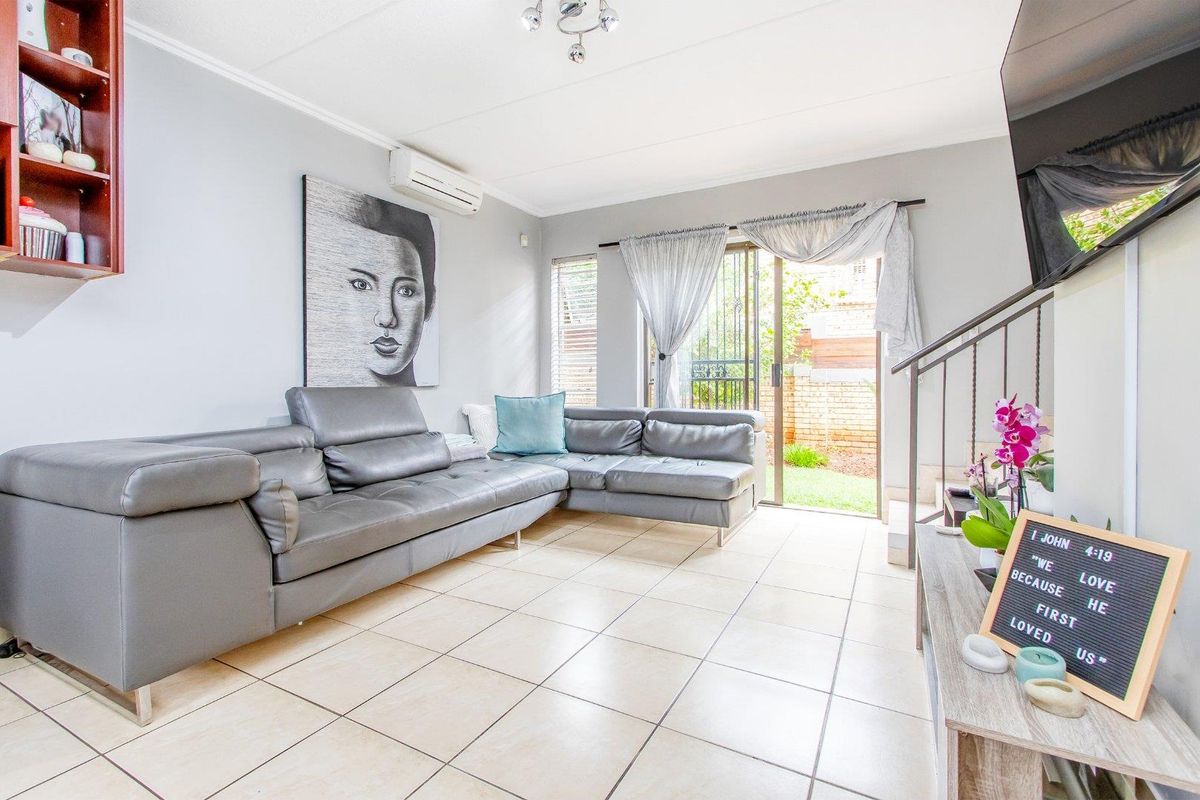 A bright living room featuring tiled flooring, a wall-mounted air conditioning unit, and sliding glass doors providing direct access to the rear garden area.