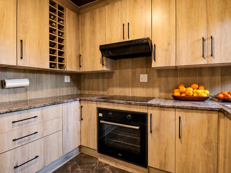 Modern kitchen featuring light wood-grain cabinetry, dark stone-look countertops, built-in oven, electric hob, and integrated wine storage.