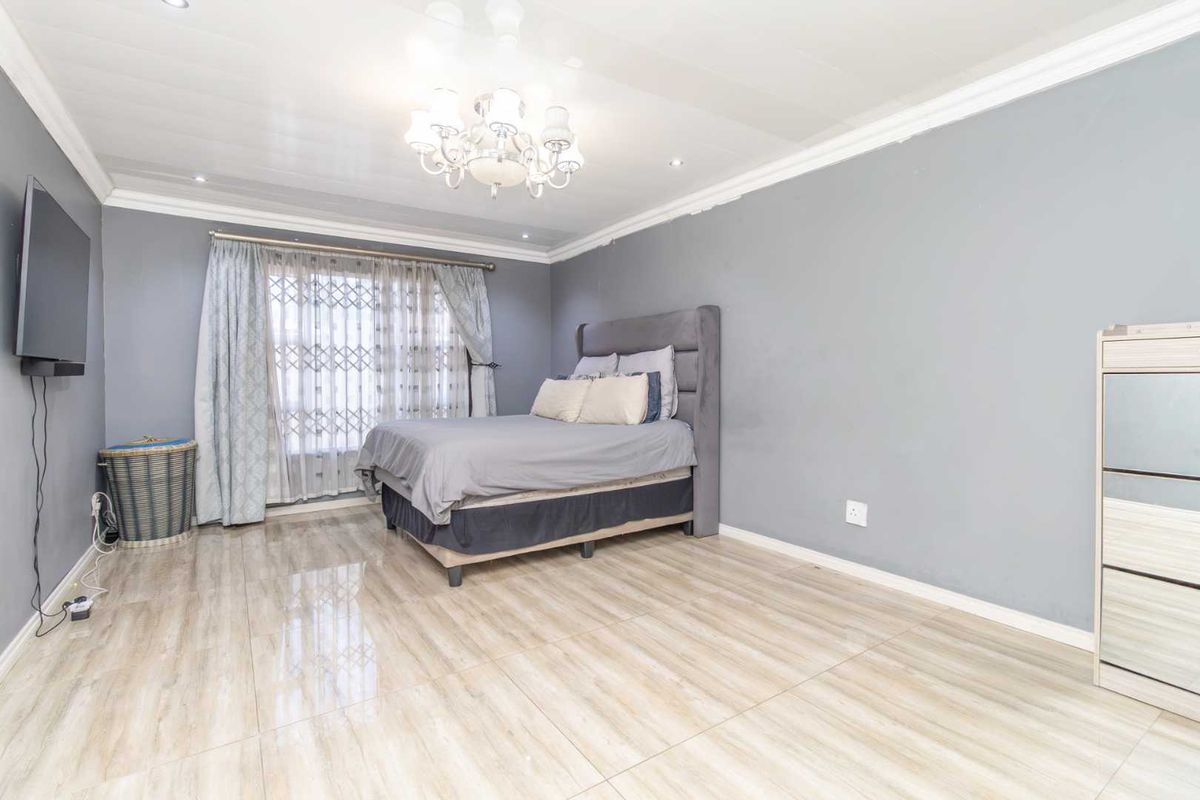 A spacious bedroom featuring light-toned tiled flooring, grey painted walls, decorative ceiling cornice, and recessed lighting.