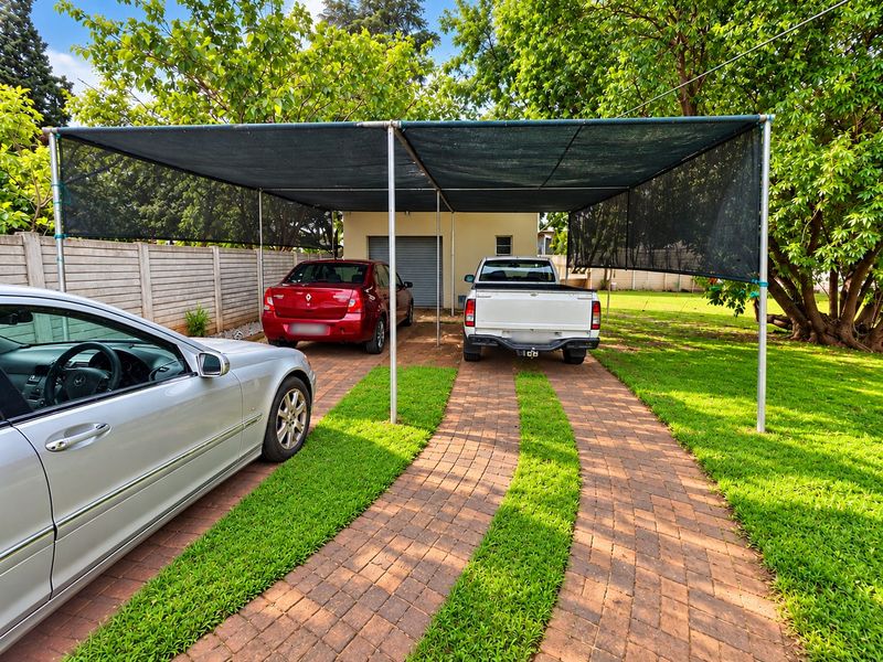 Front exterior view featuring a paved driveway with integrated lawn strips, a shade cloth carport structure, and a detached garage.
