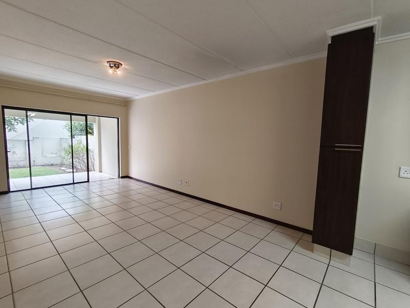 A spacious, empty living area featuring neutral tiled flooring, a built-in dark wood cabinet, and large sliding glass doors leading to an outdoor space.
