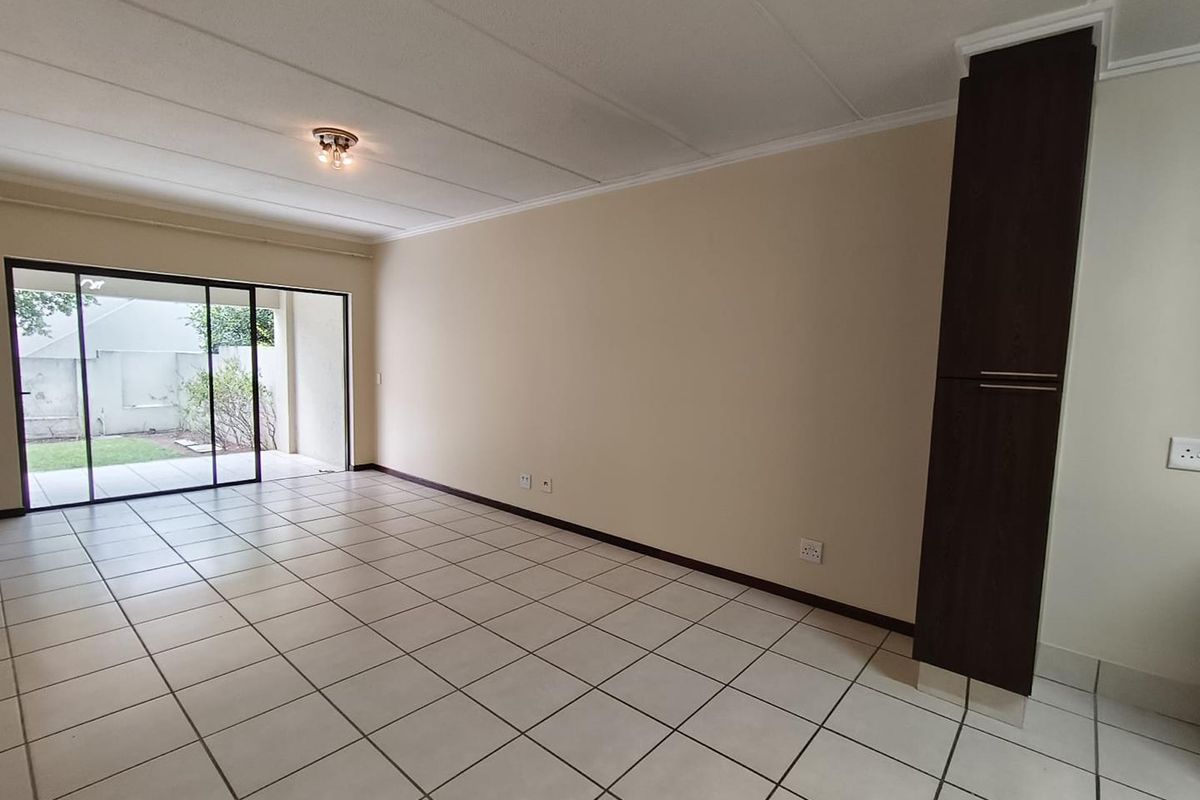 A spacious, empty living area featuring neutral tiled flooring, a built-in dark wood cabinet, and large sliding glass doors leading to an outdoor space.