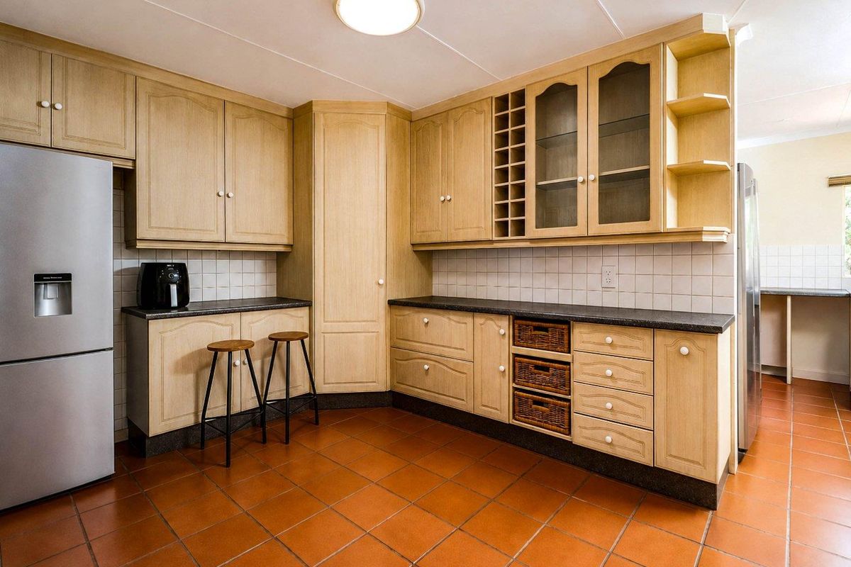 A functional kitchen featuring light wood-toned cabinetry, dark laminate countertops, a tiled splashback, and durable terracotta floor tiles.