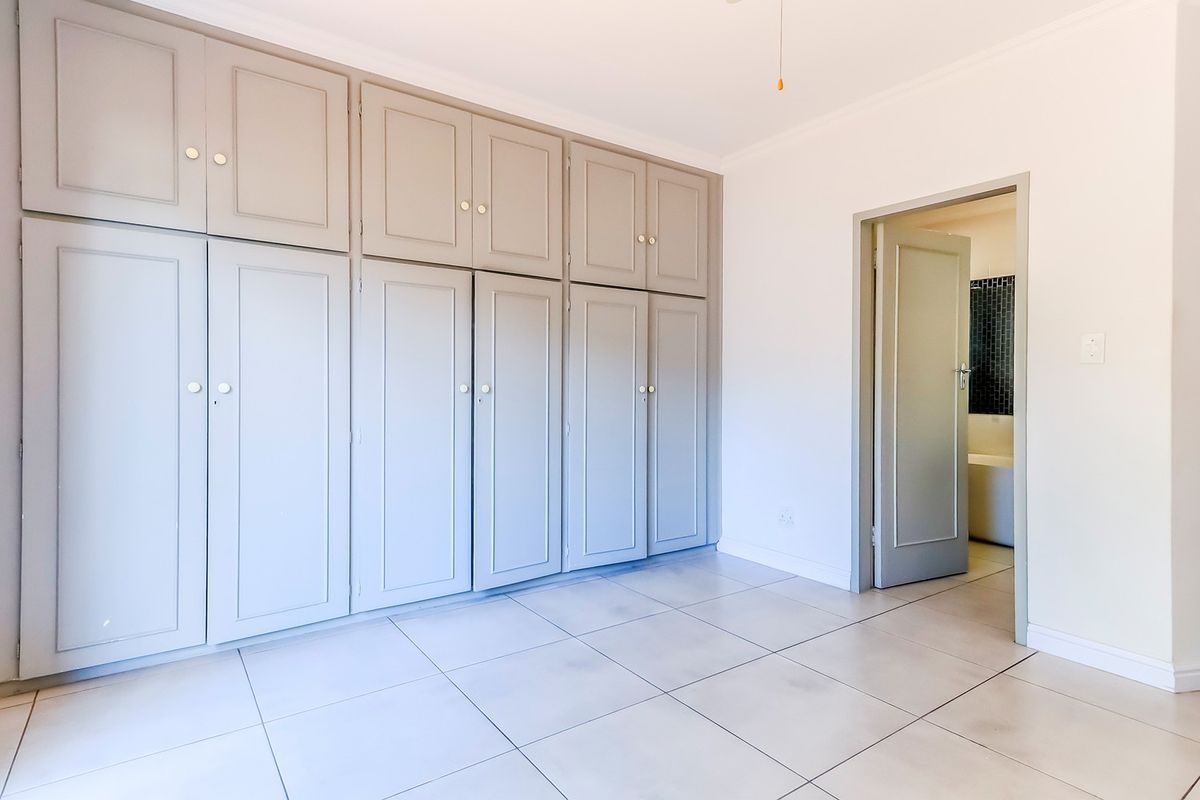 A bright, empty bedroom featuring extensive built-in cupboards, neutral tiled flooring, and a doorway leading to an adjacent bathroom.