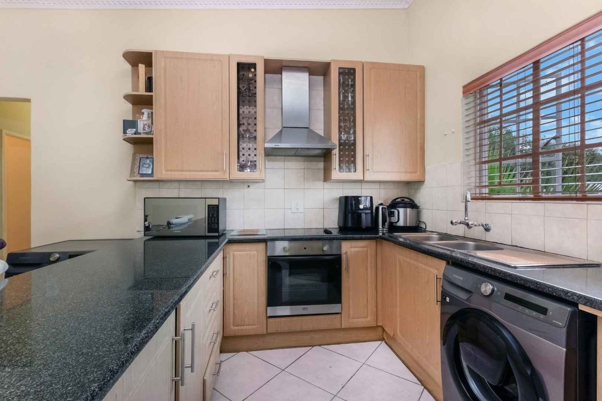 Functional kitchen featuring light wood cabinetry, dark granite countertops, stainless steel extractor fan, built-in oven, and integrated laundry plumbing.