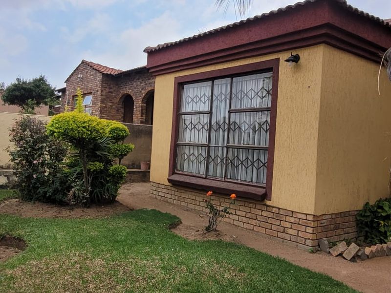Rear view of the property featuring a yellow plastered facade, brick base, and security-gated window overlooking a private garden area.