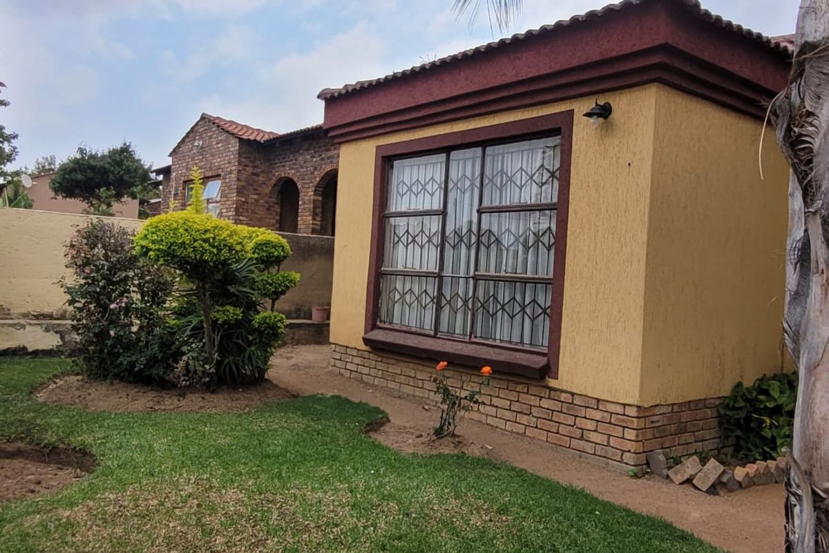 Rear view of the property featuring a yellow plastered facade, brick base, and security-gated window overlooking a private garden area.