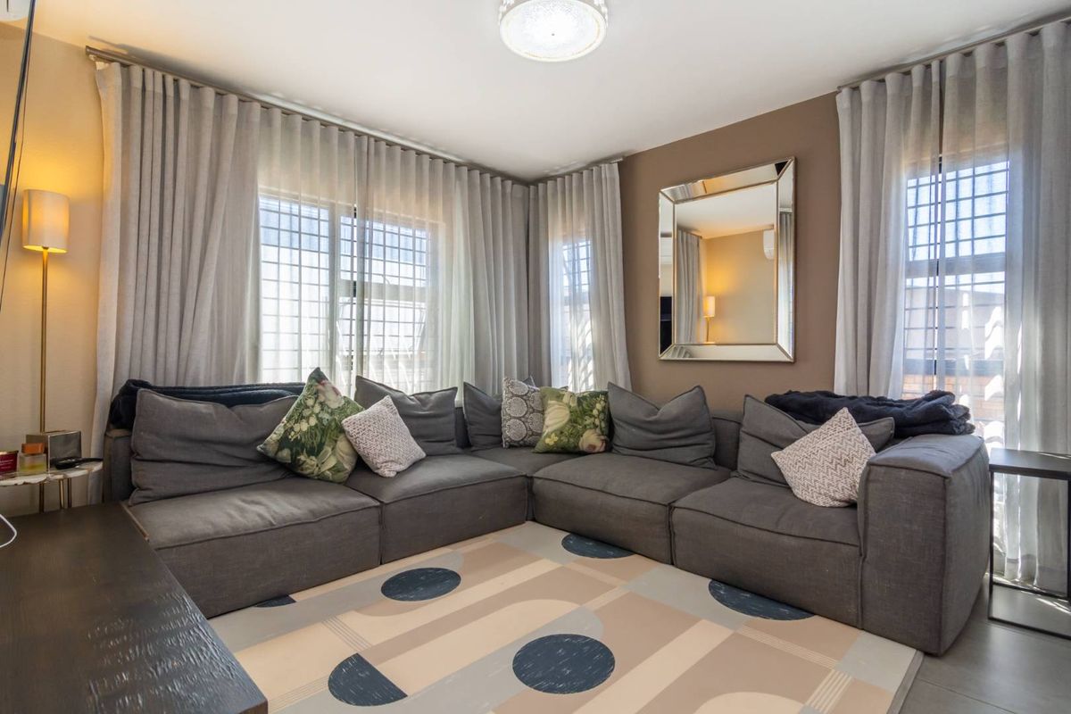 A comfortable living room featuring large windows with security bars, neutral wall tones, and tiled flooring, creating a bright and inviting space.