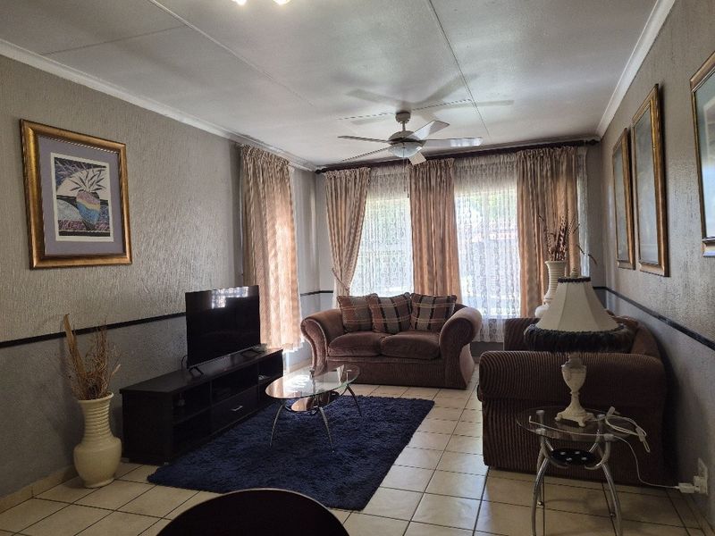 A comfortable living room featuring tiled flooring, a ceiling fan, and a dado rail, providing a functional and well-defined space for relaxation.