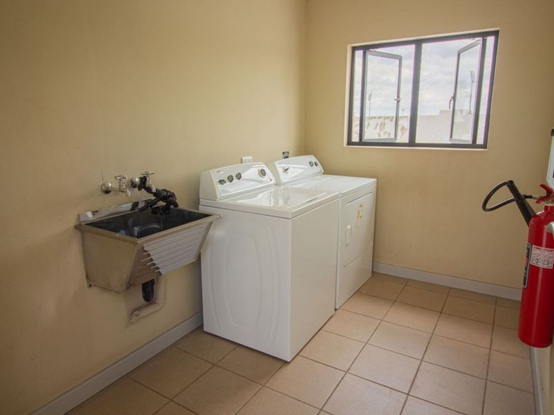 A functional laundry room featuring tiled flooring, a stainless steel utility sink, and a casement window for natural light.